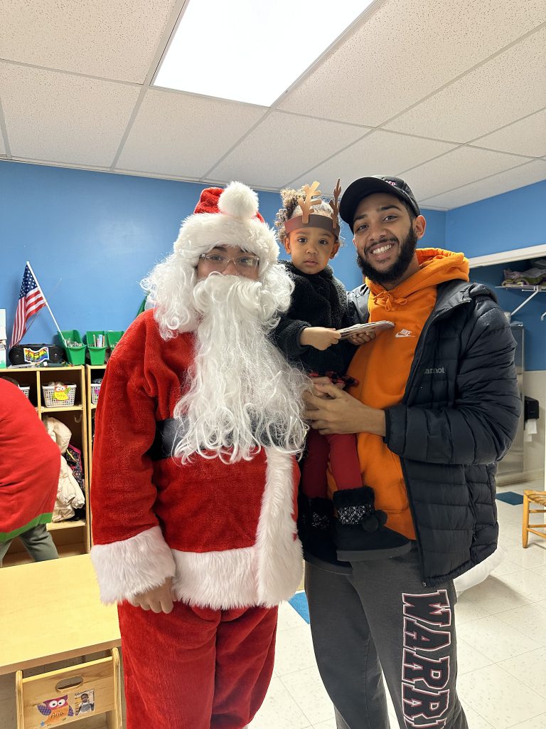 Parent holding their daughter and smiling for a photo with Santa Claus.