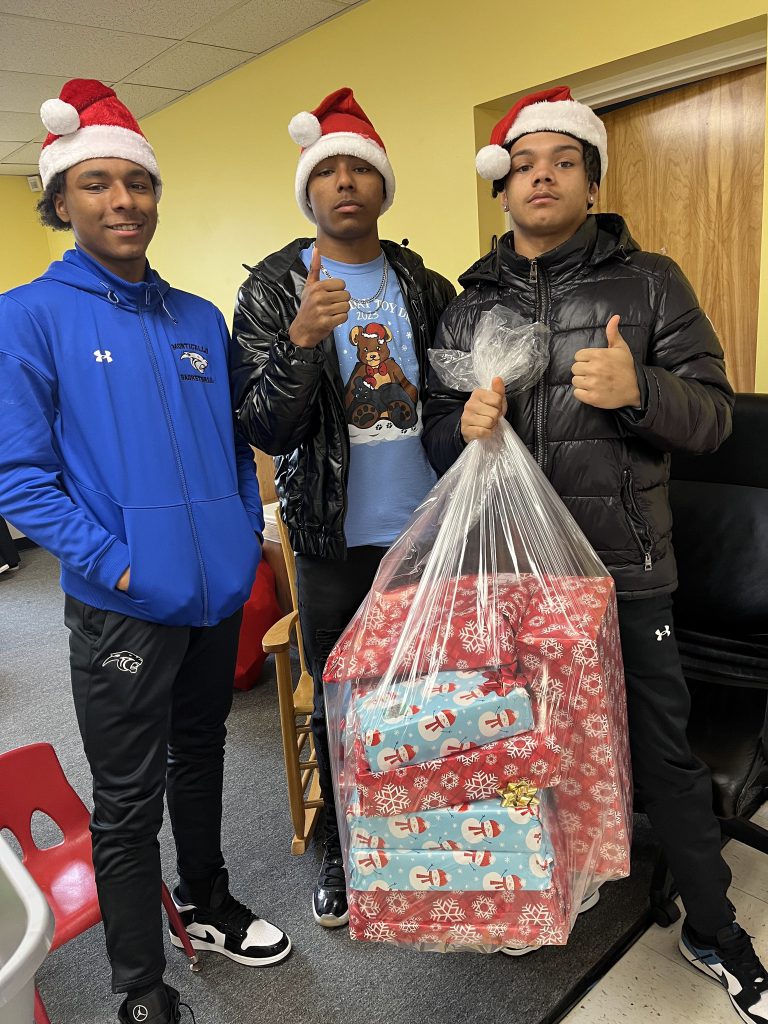 Three students wearing Santa hats with one holding a bag full of presents in his hand.