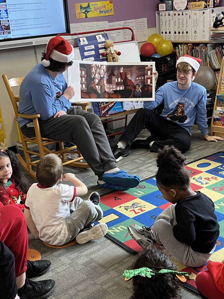 Two high school students reading to children in a classroom.