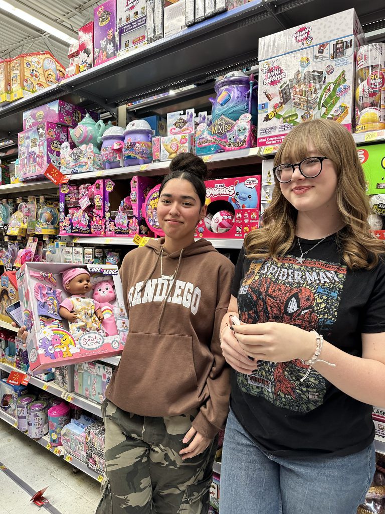 Two students smiling with toys on shelves in the background.