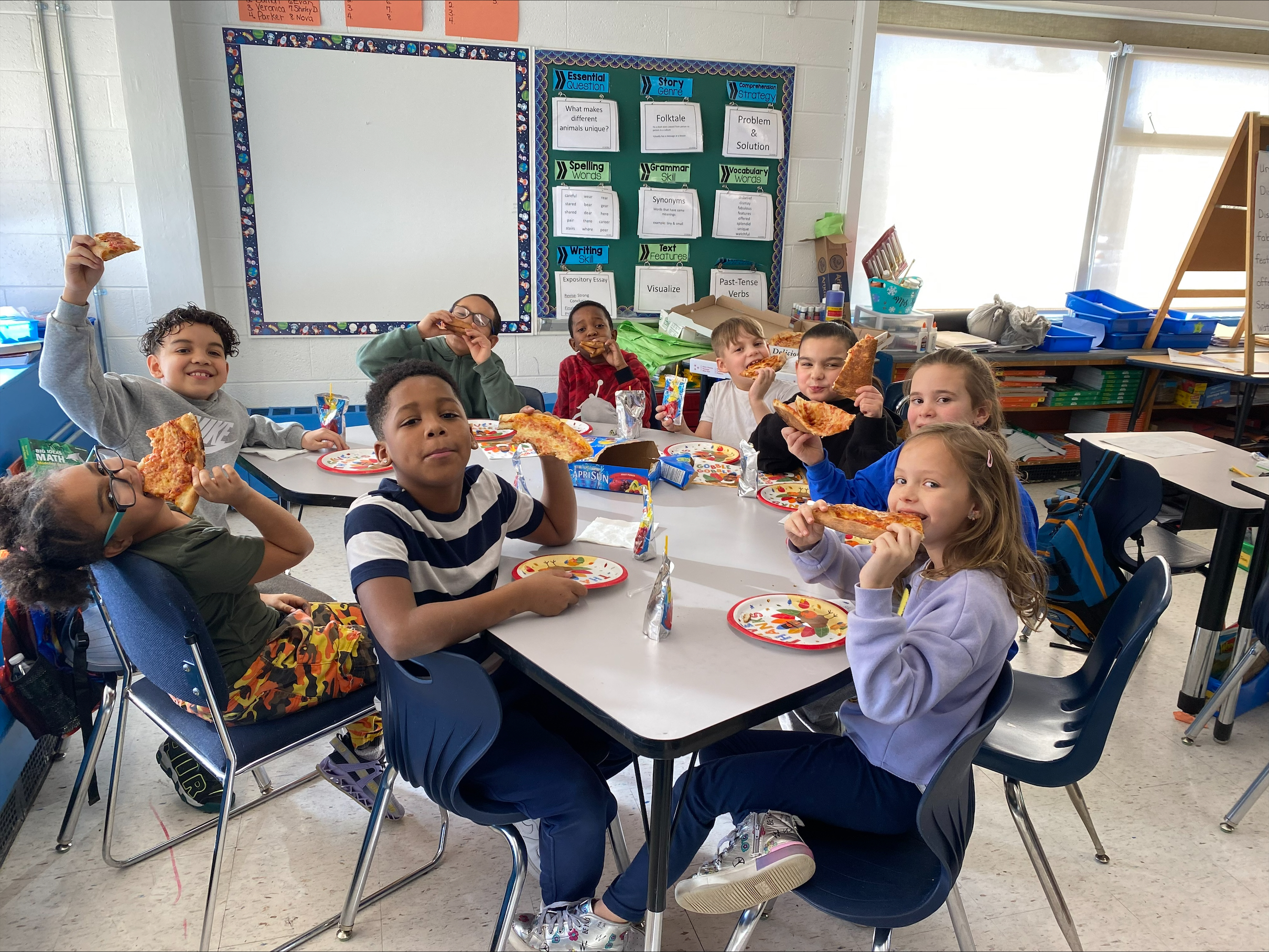 a group of students are seated at a table eating pizza