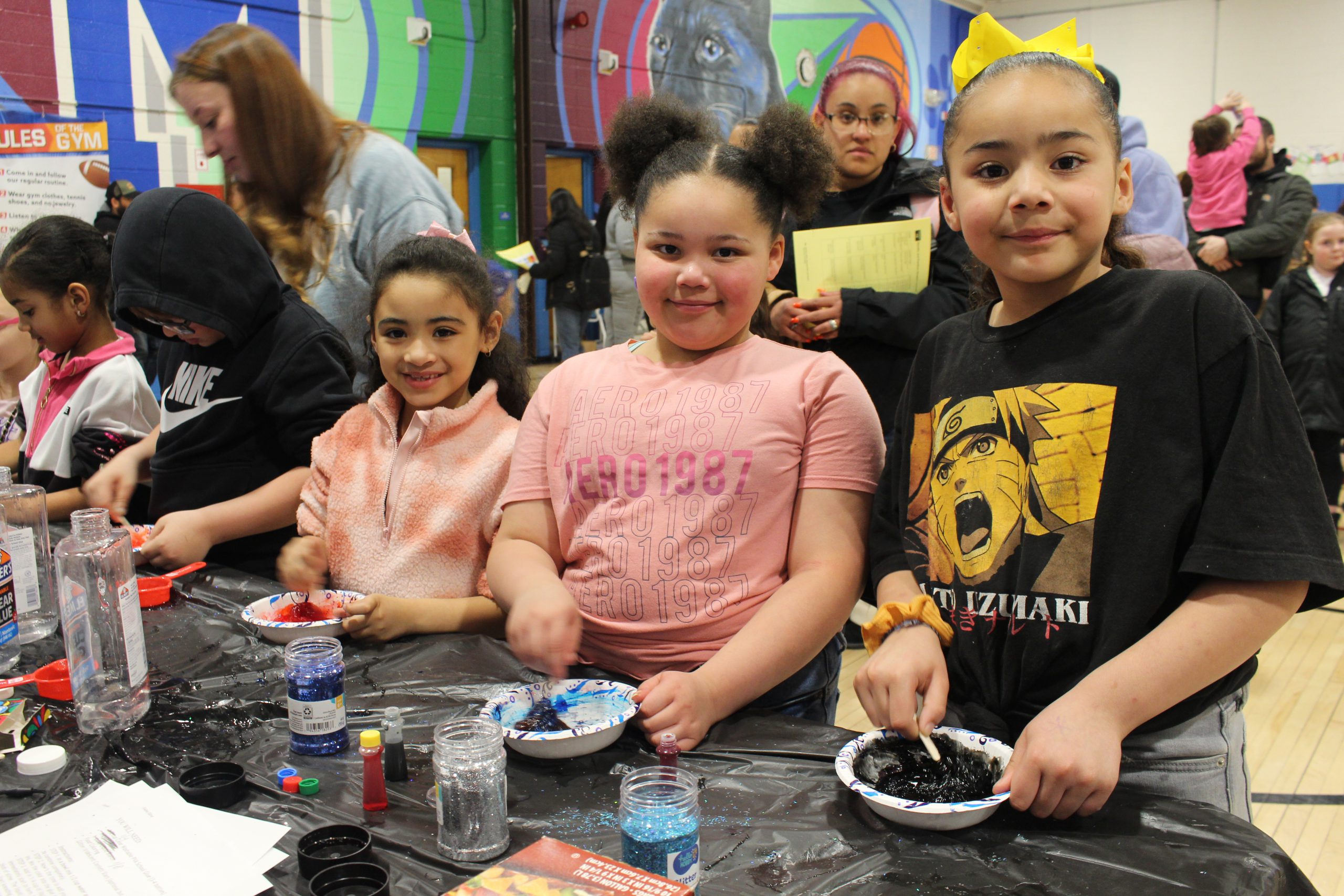 three elementary students are mixing slime at a table 