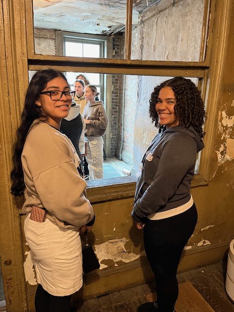 two female students are posing near a window at the tenement museum 