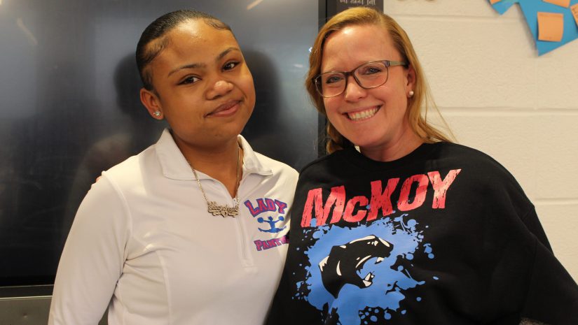 a teacher is posing with a student and holding up a shirt that she received.