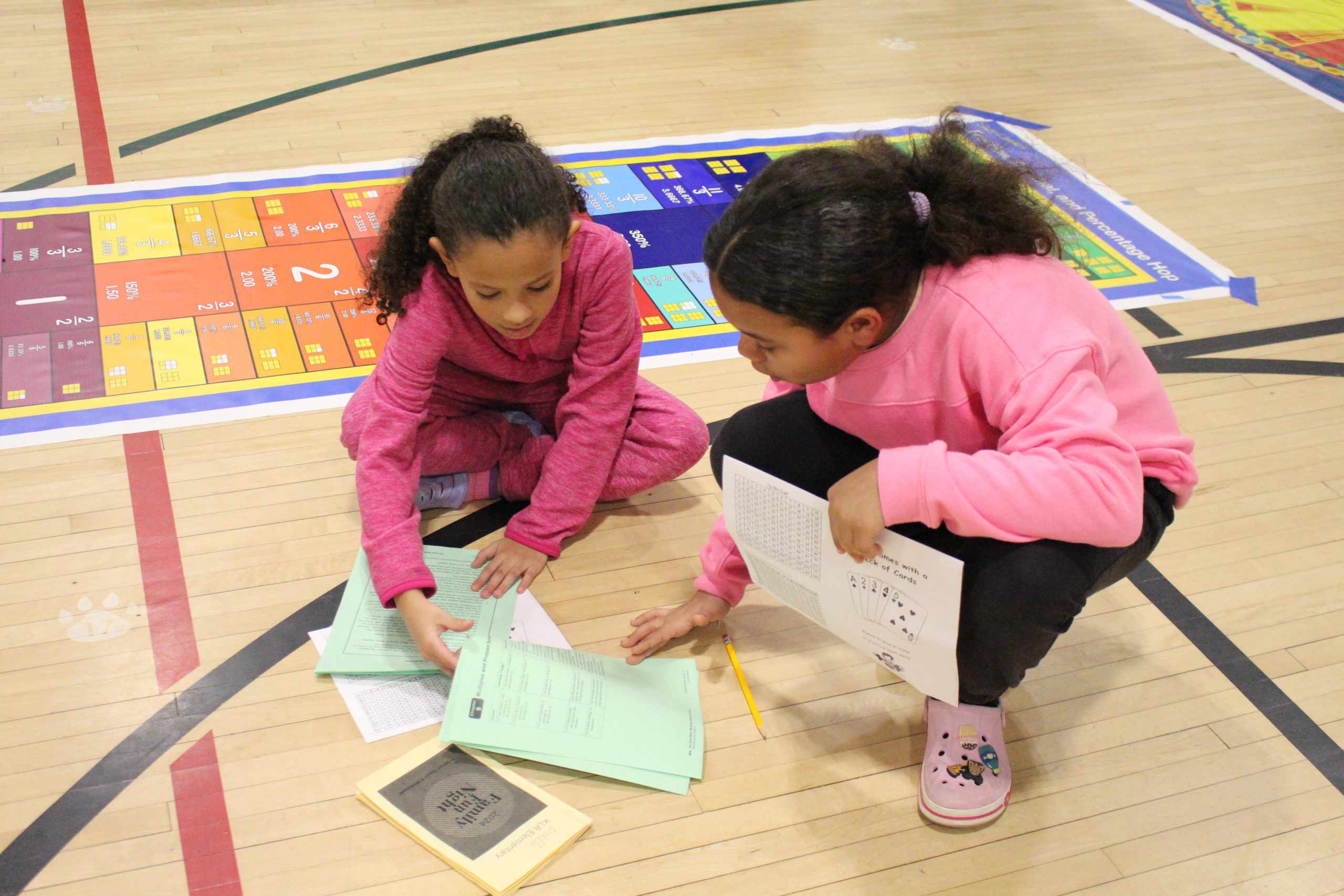 two girls are kneeling on the gym floor working on a math problem. 