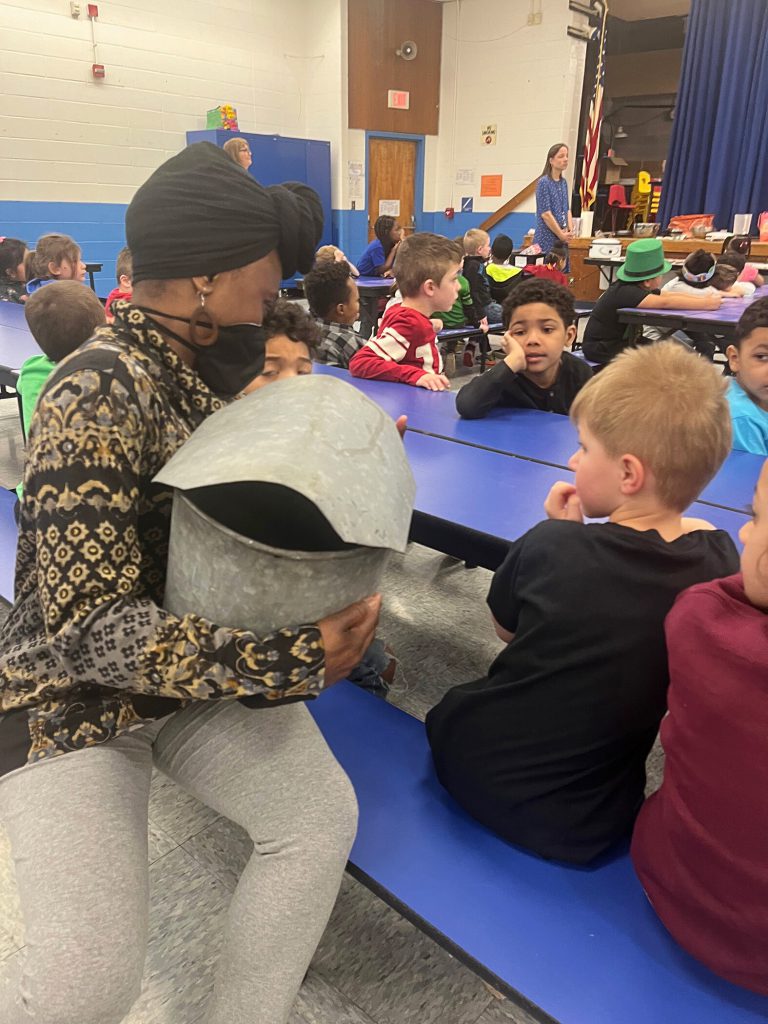 Teacher showing elementary students the metal bucket used for tapping syrup from trees.