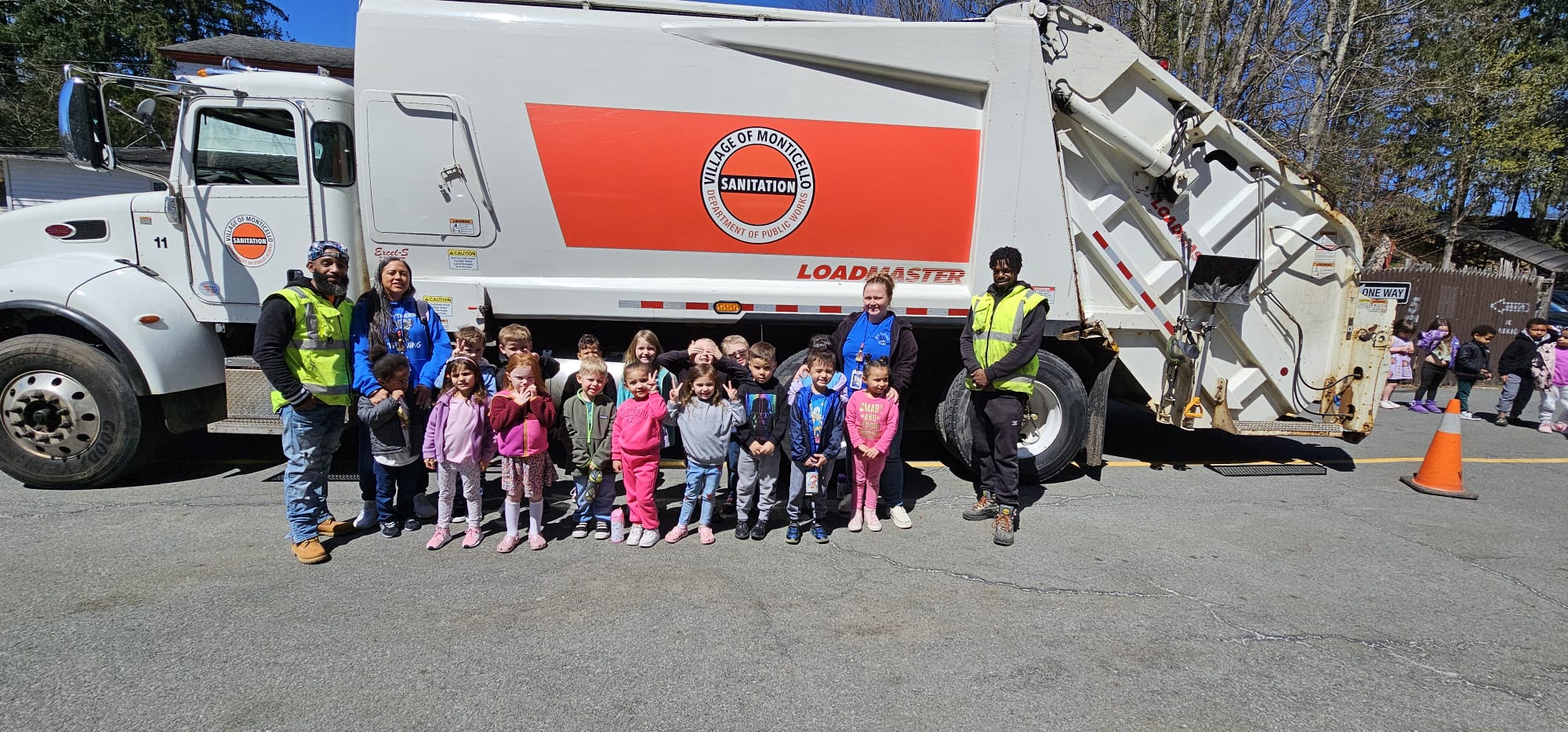 Two sanitation workers pose with preschoolers and their truck 