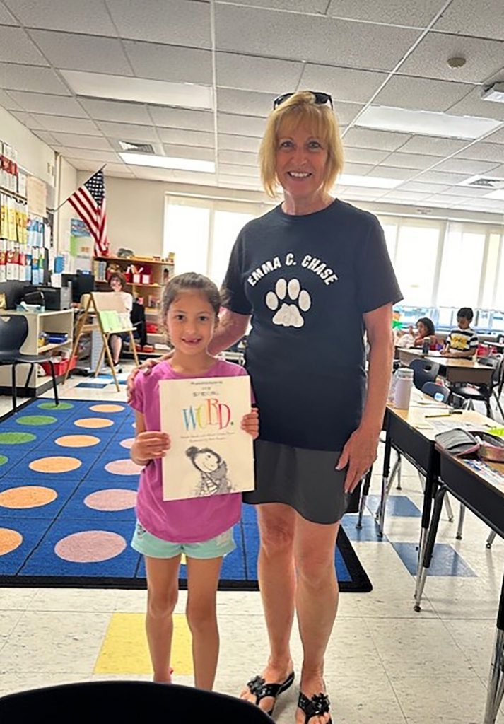 A student holding her poster and smiling for a photo with a school staff member.