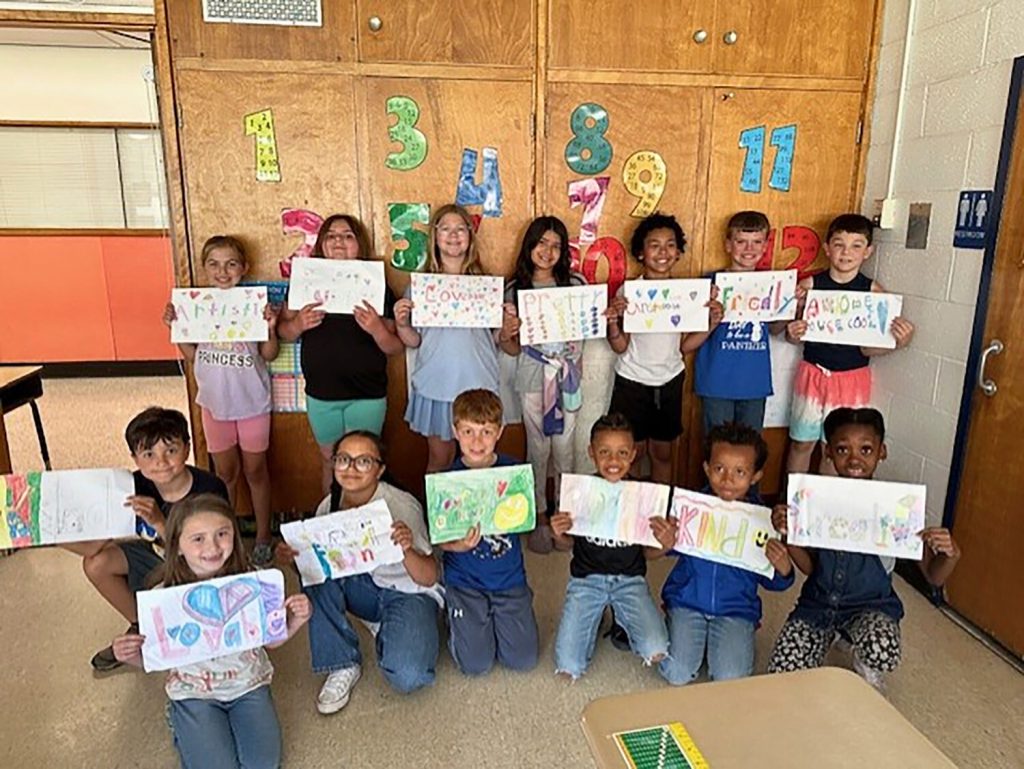 Class group photo. Students are holding their posters and smiling for a group photo.