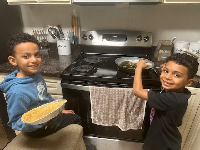 two children are standing at the stove in the middle of cooking 