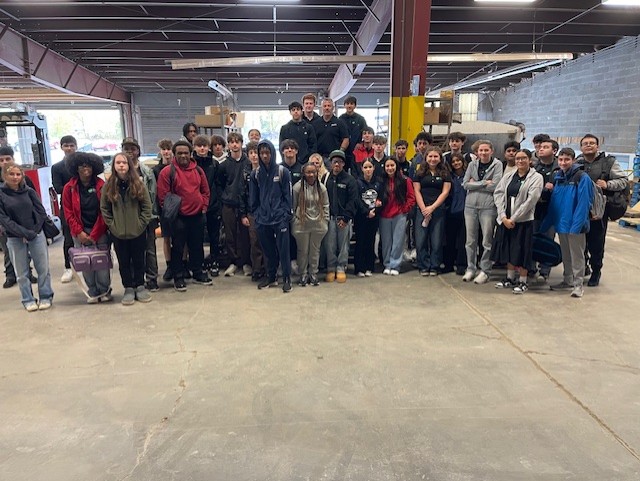 students pose inside the warehouse with workers 