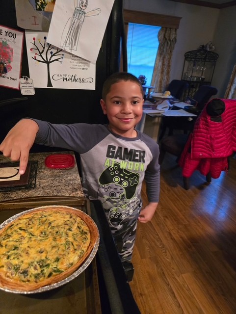 Capone McCalla smiles for the camera in his kitchen. On the counter is the quiche he and his family baked as part of the workshop