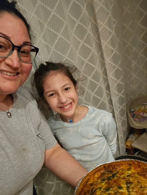 a mother and daughter smile for the camera, holding the quiche that they baked togather. 