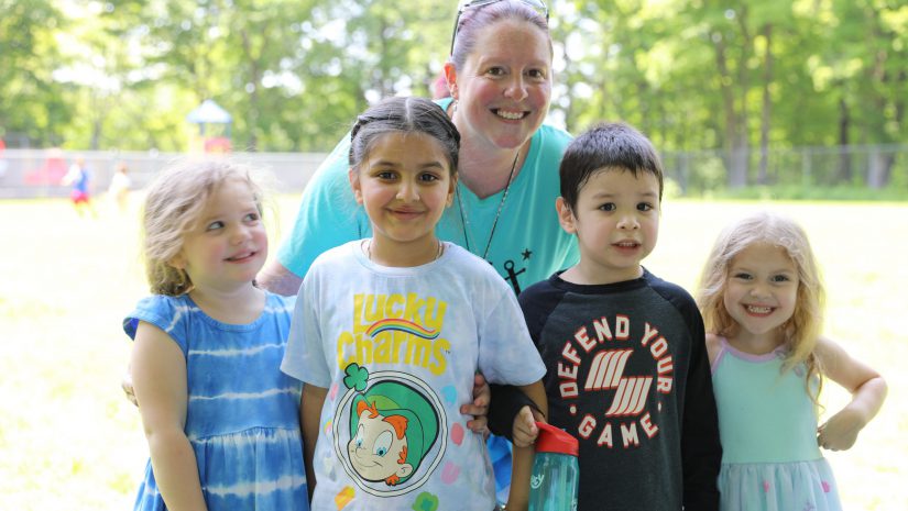 a group of preschoolers are posing with their teacher in the playground