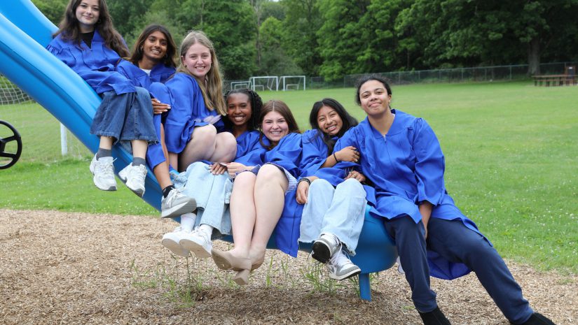 a group of senior students are in graduations gowns playfully sitting on a slide