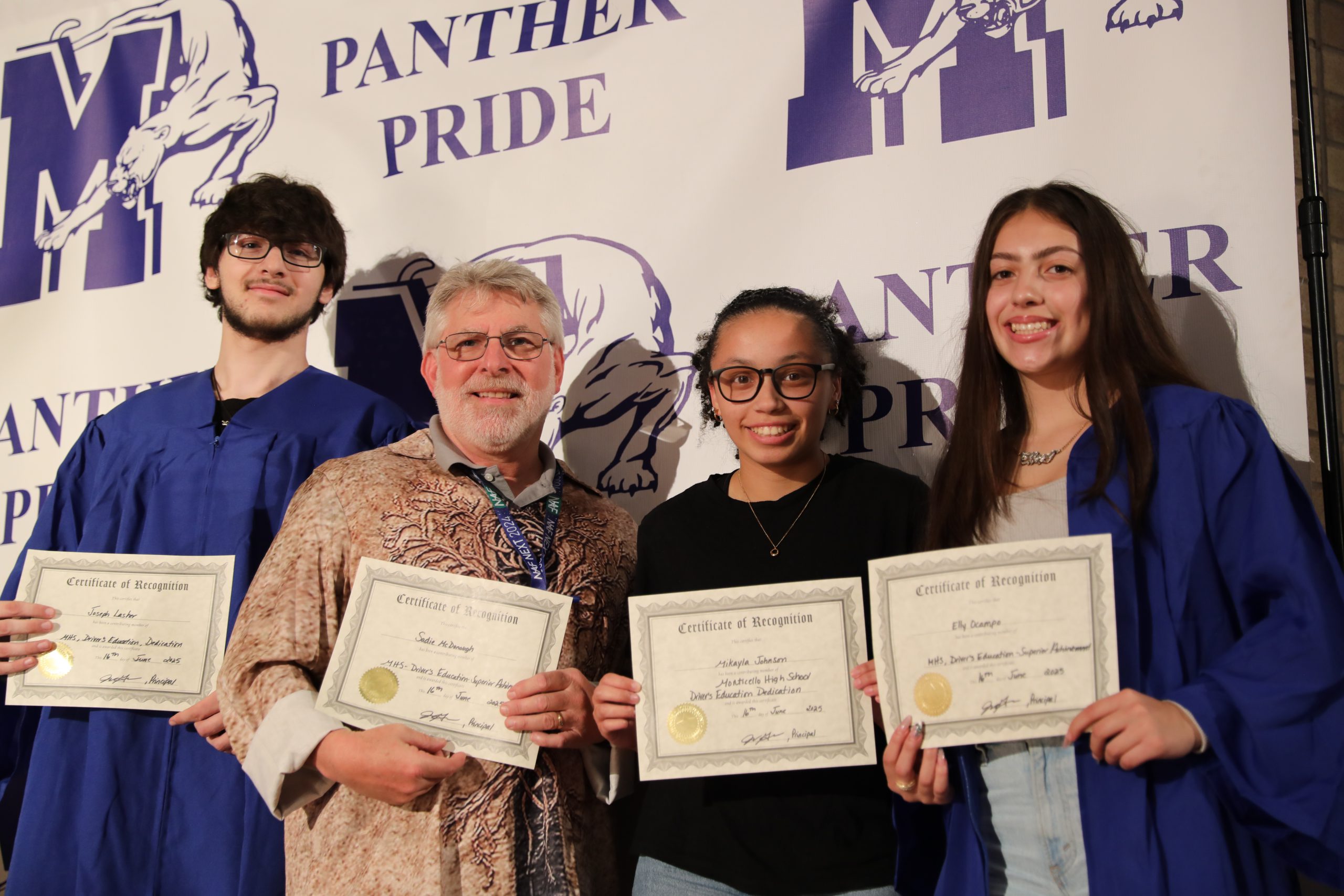 a group of students pose in front of a backdrop. They are smiling and holding their certificates 