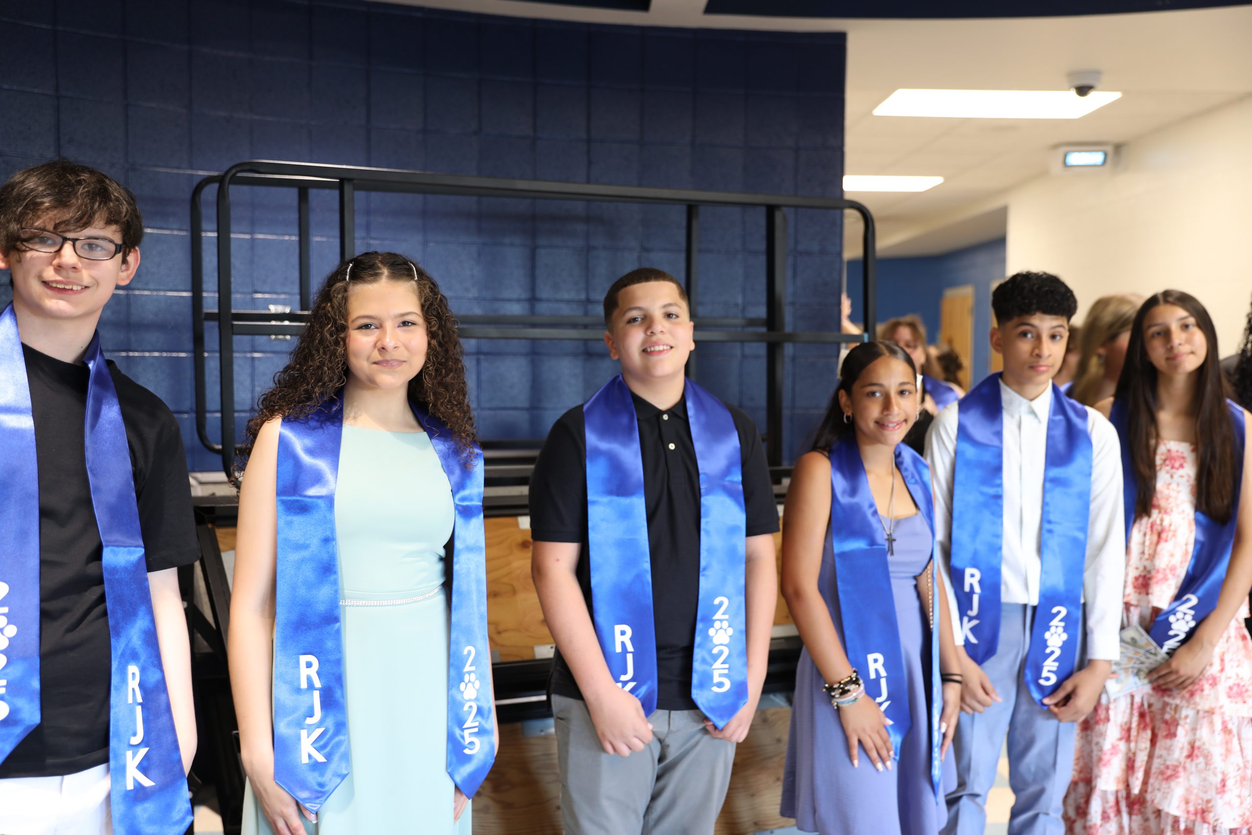 a group of students wearing blue sashes are posing in the hallway. 