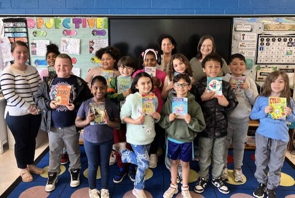 a group of second graders are posing and holding up donated books