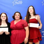 students are posing in front of a backdrop holding their awards