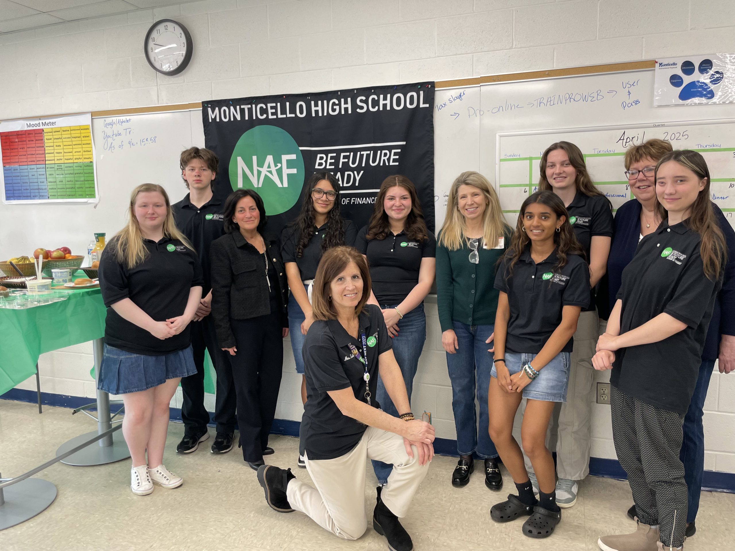 a group of students from the AOF pose in front of the AOF banner in a classroom