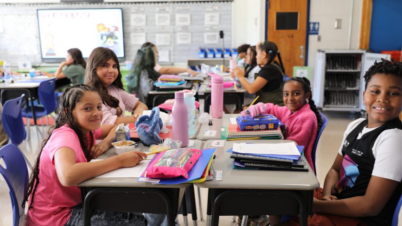 a group of students are seated around a desk, smiling