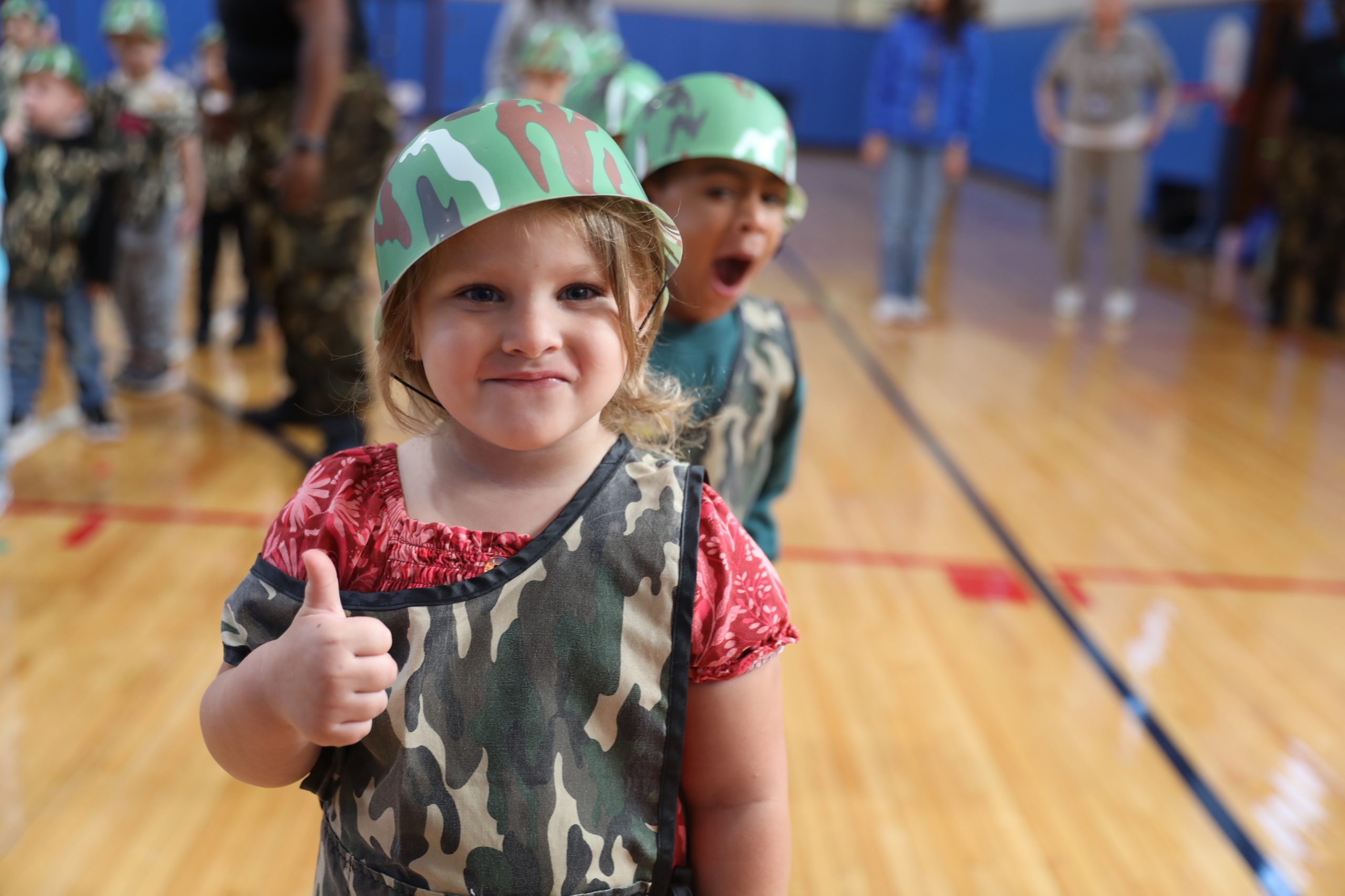 a preschooler is wearing a military vest and helmet and giving a thumbs up 