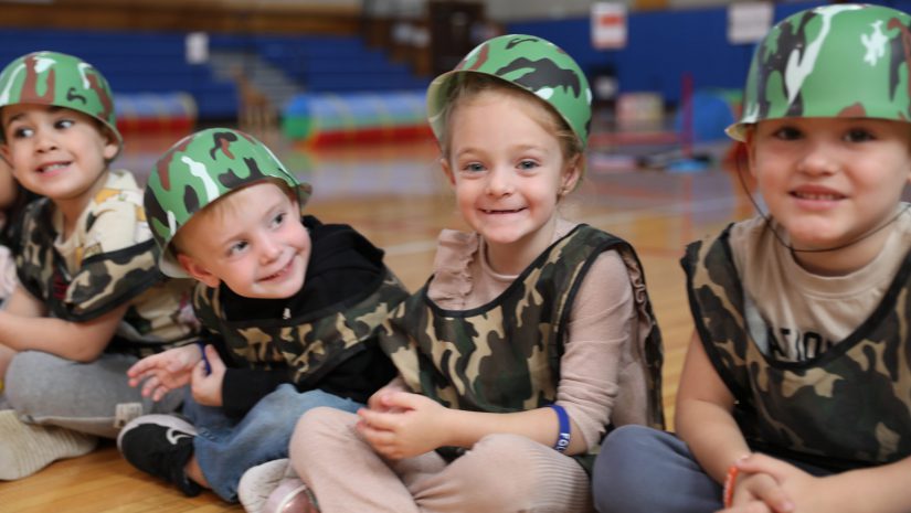 four students in military vests and helmets are smiling for the camera.