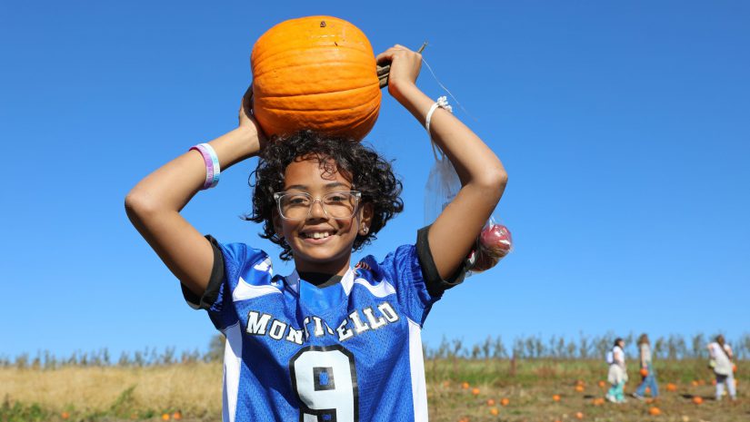 a student wearing a Monticello jersey holds a pumpkin over his head