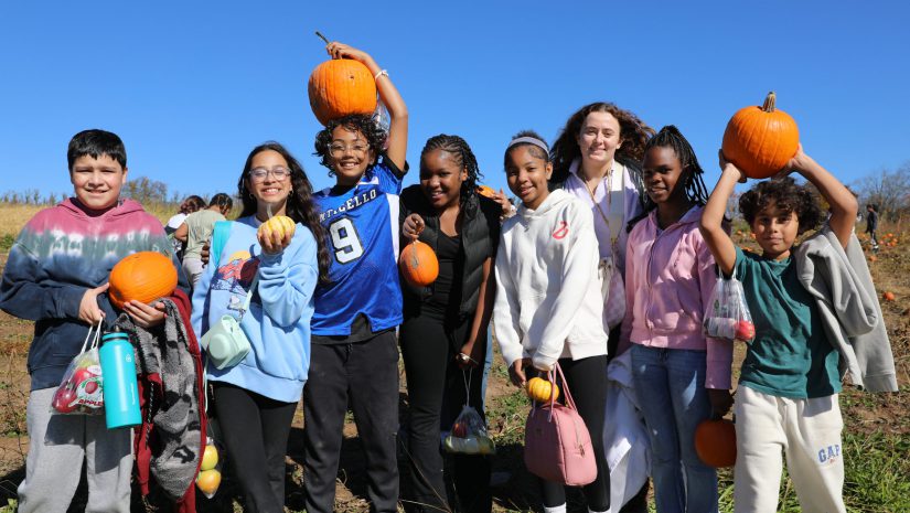 a group of students are holding pumpkins and posing on a farm