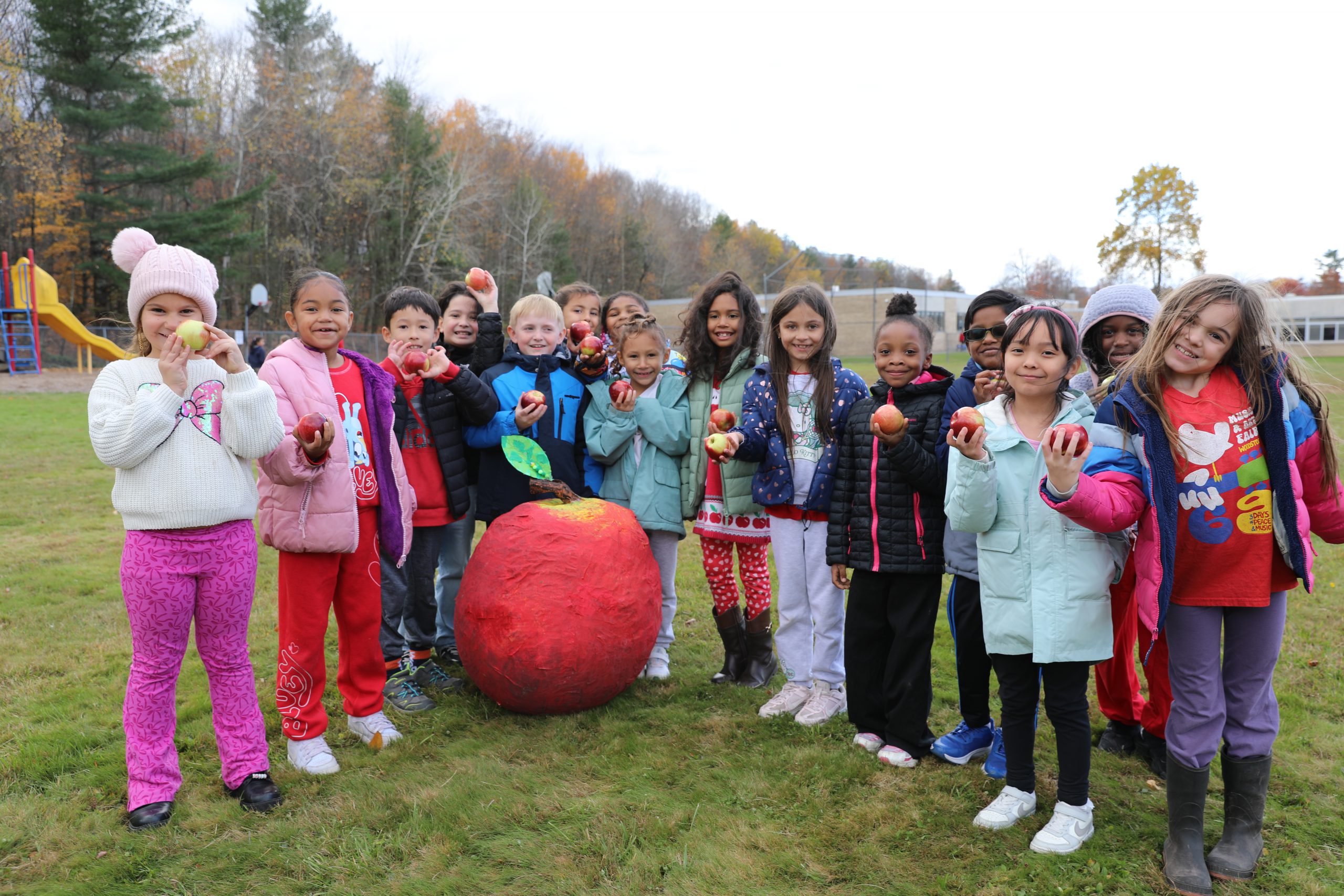 a group of students stand around a large paper mache apple