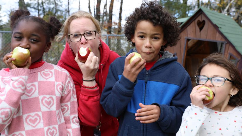 3 students and a teacher are crunching into an apple
