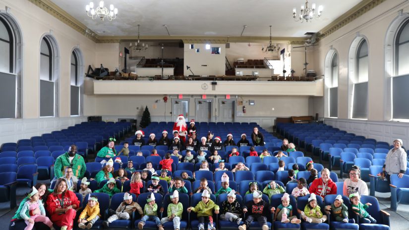 students and staff members dressed as grinches are seated in the auditorium