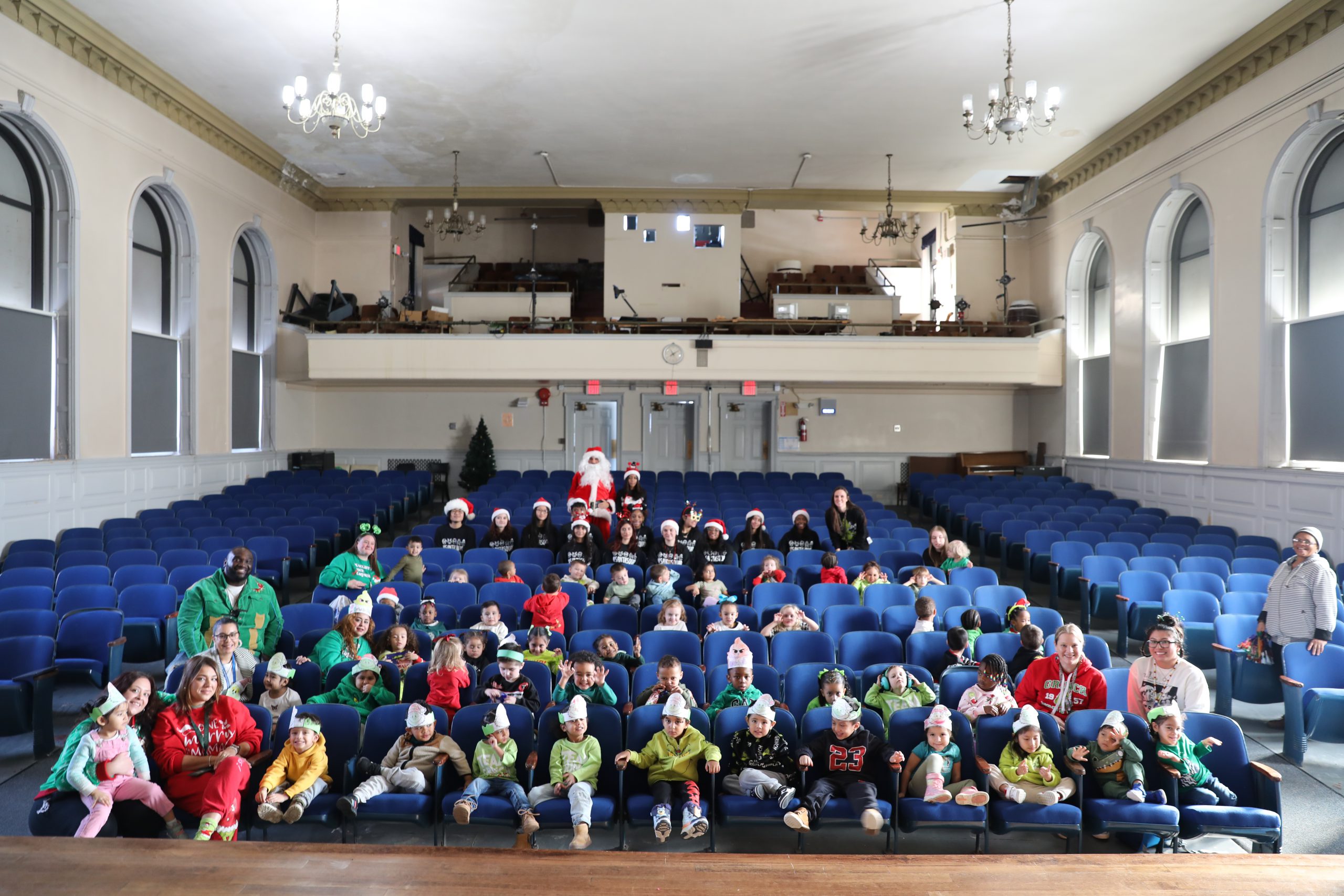 students and staff members dressed as grinches are seated in the auditorium
