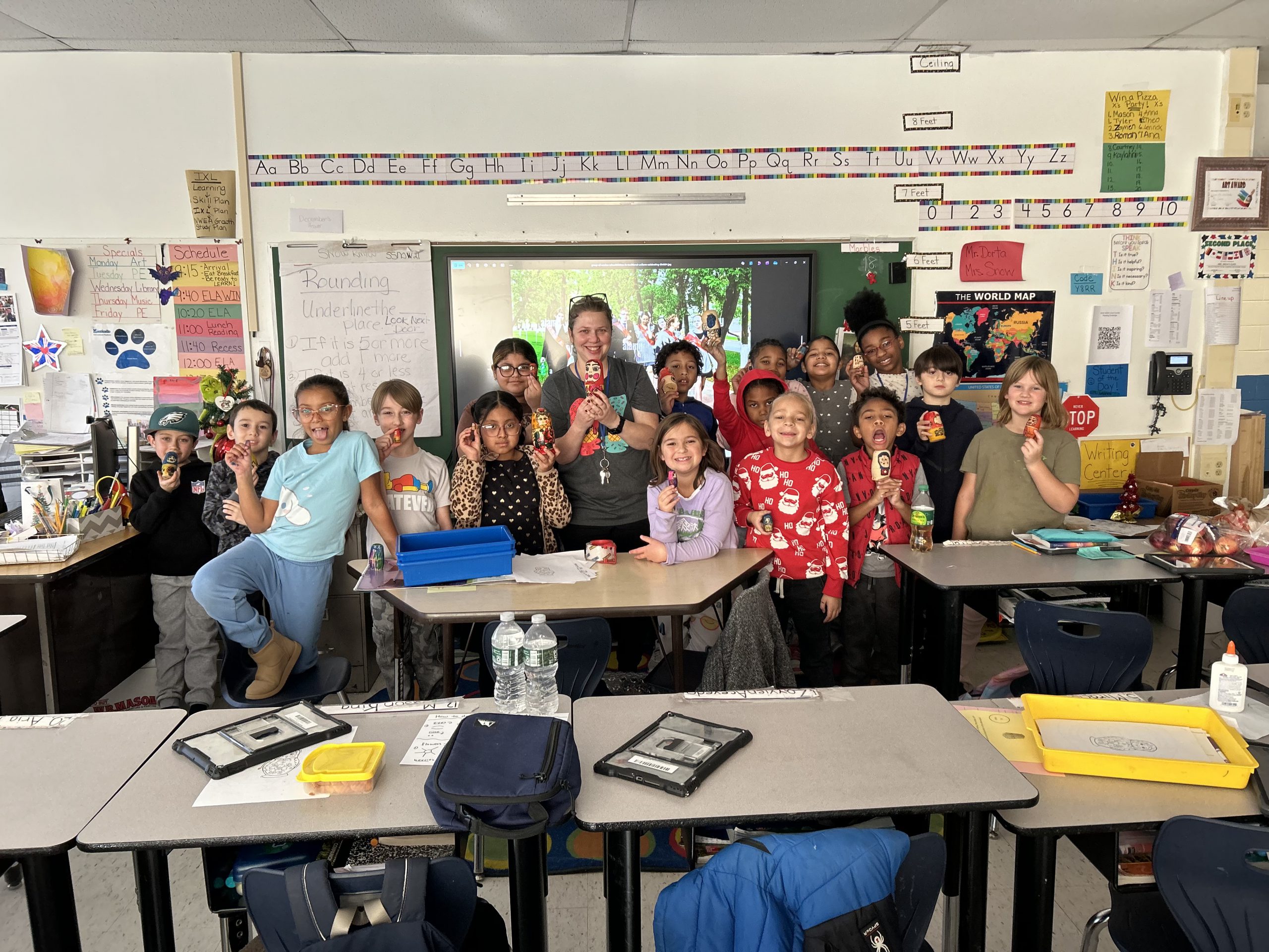 Ms. Snow's students are posing with their art teacher who is holding a Russian doll