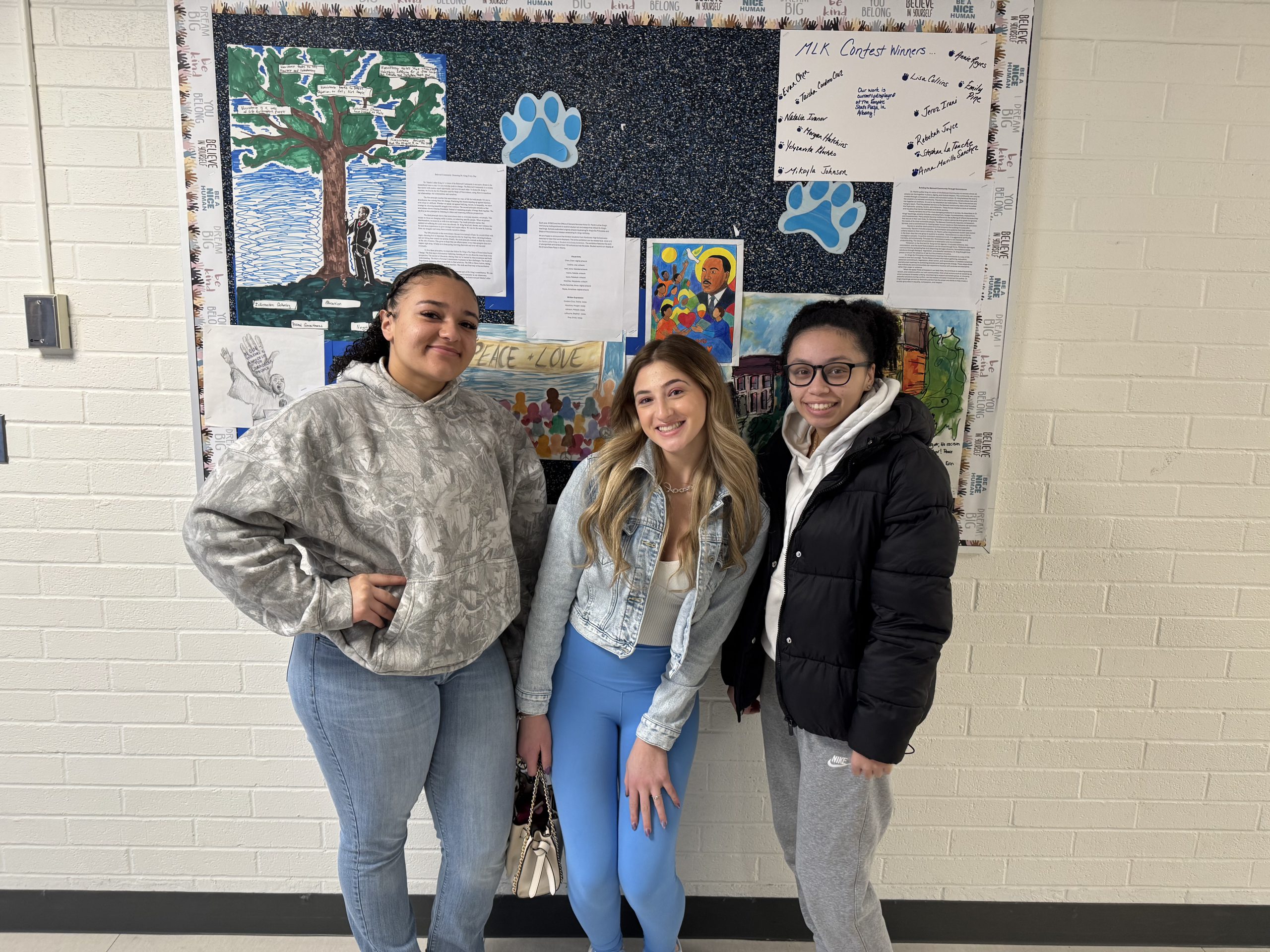 three students whose artwork was chosen for the exhibit are smiling for the camera