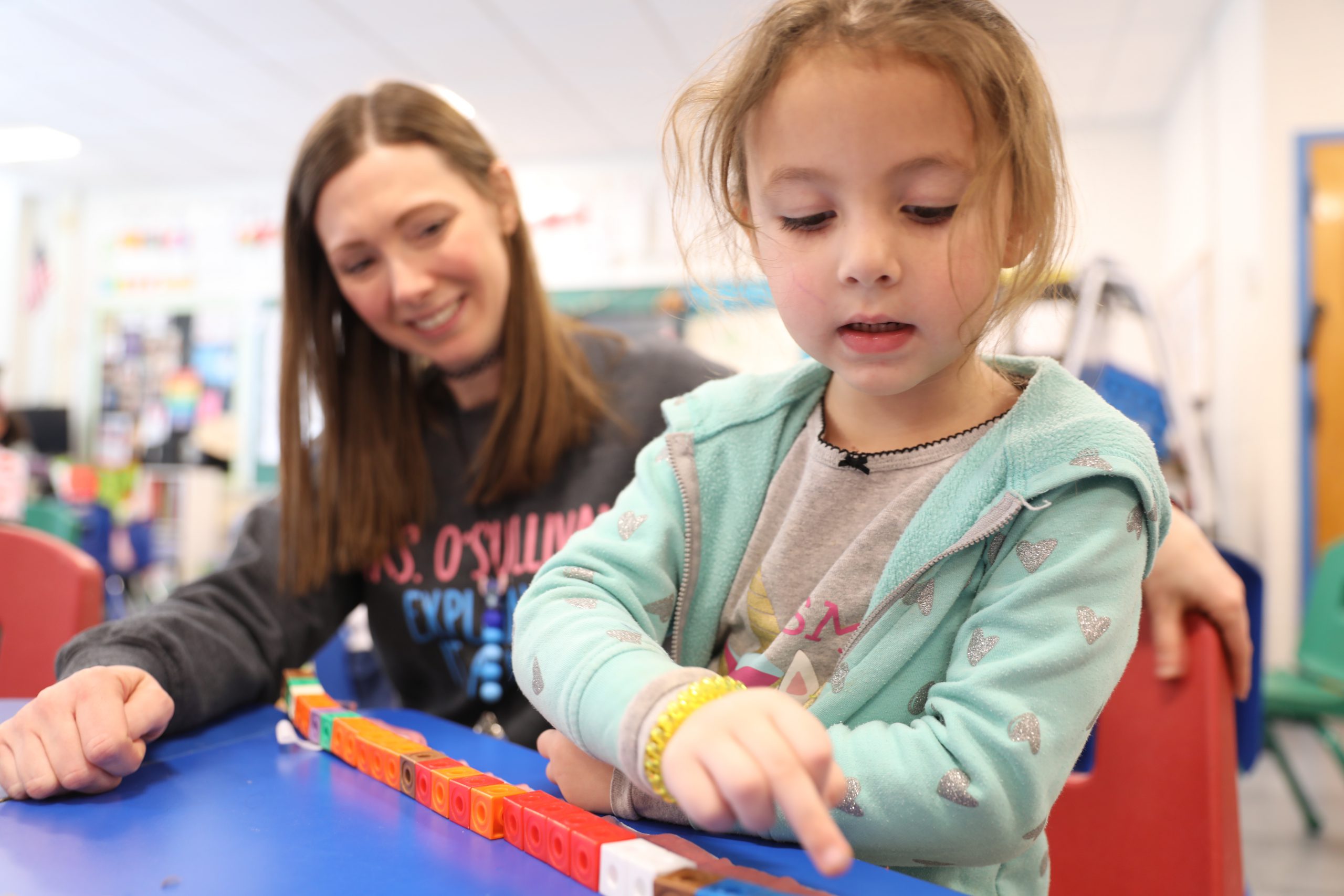 a student counts blocks against fruit by the foot as a teacher looks on