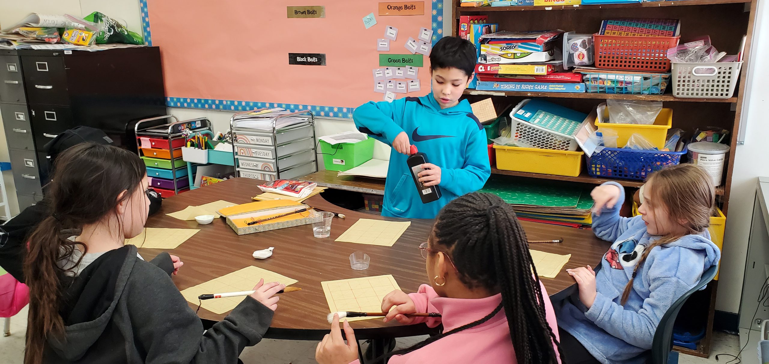 a student demonstrates how to write the Chinese character for good luck to his classmates