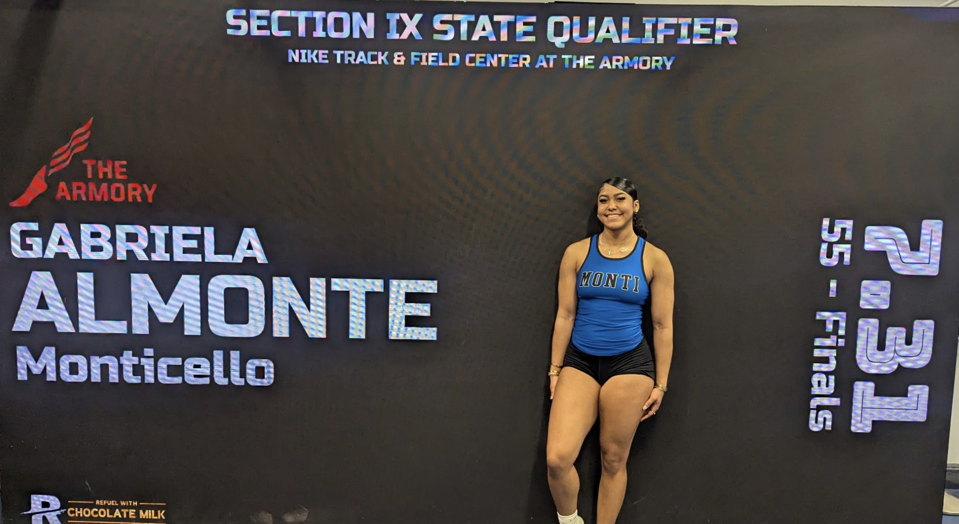 Gabby Almonte is posing in a track uniform in front of a promotional backdrop. 