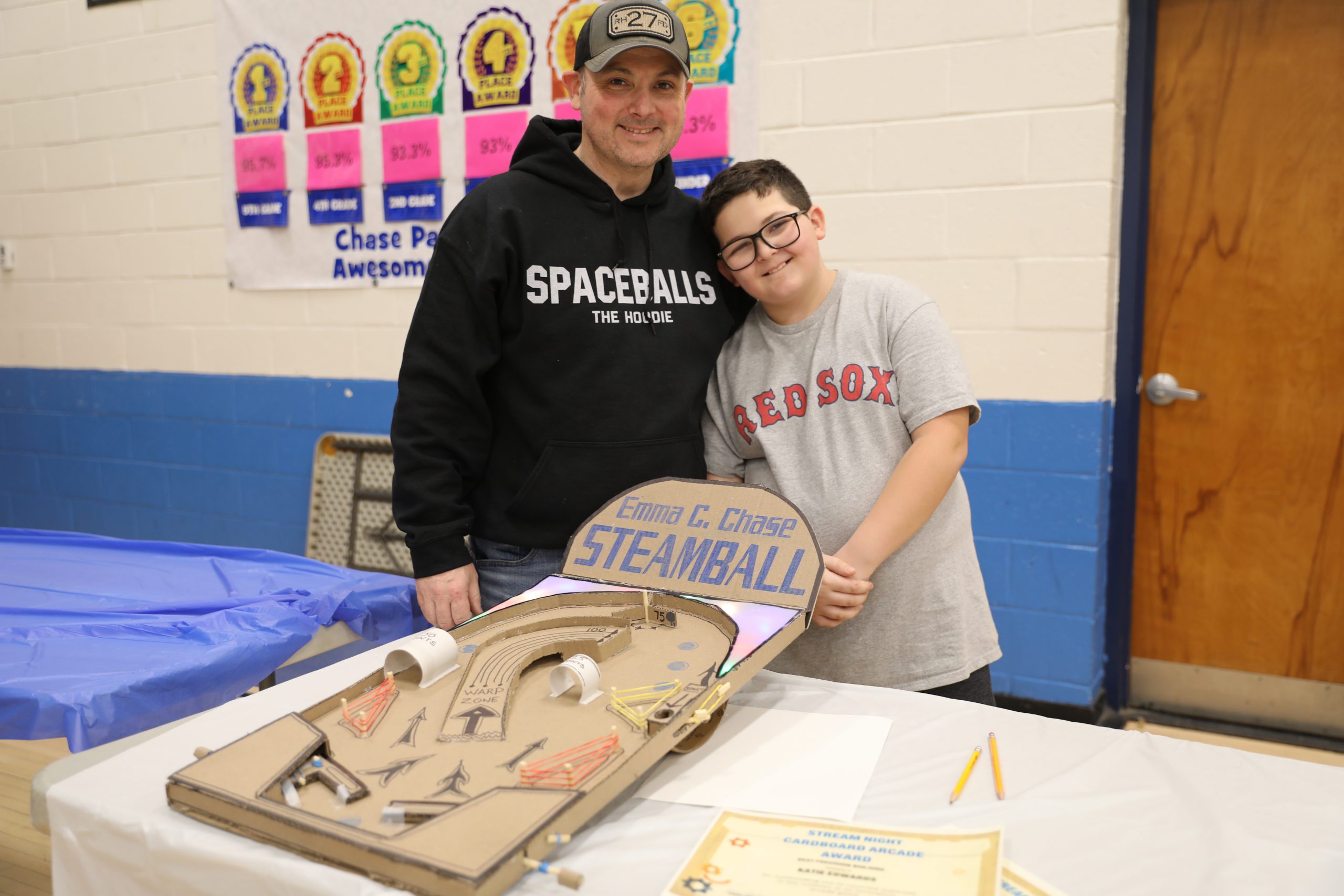 a student poses next to the game he created with his father