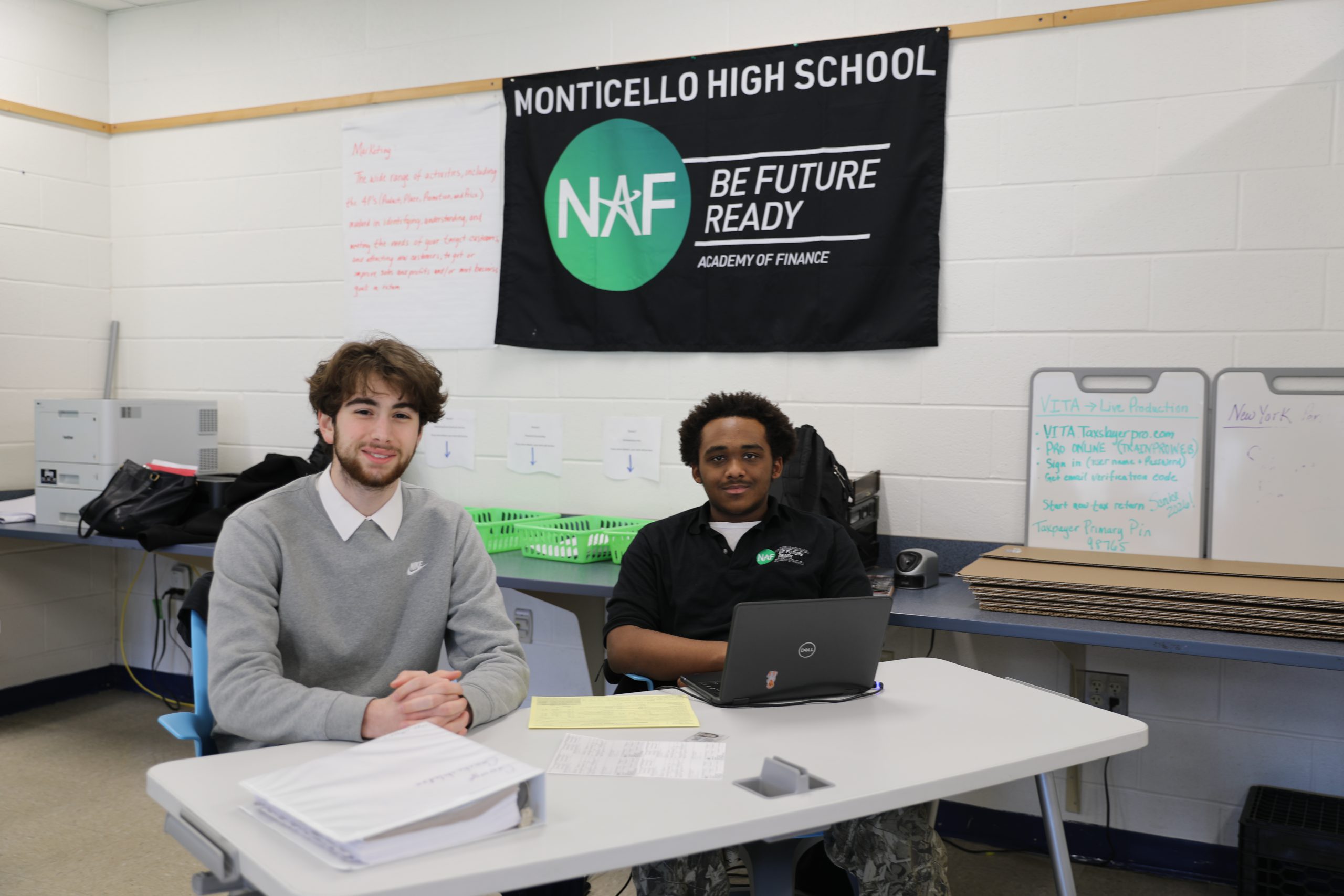 two students are seated at a desk, posing