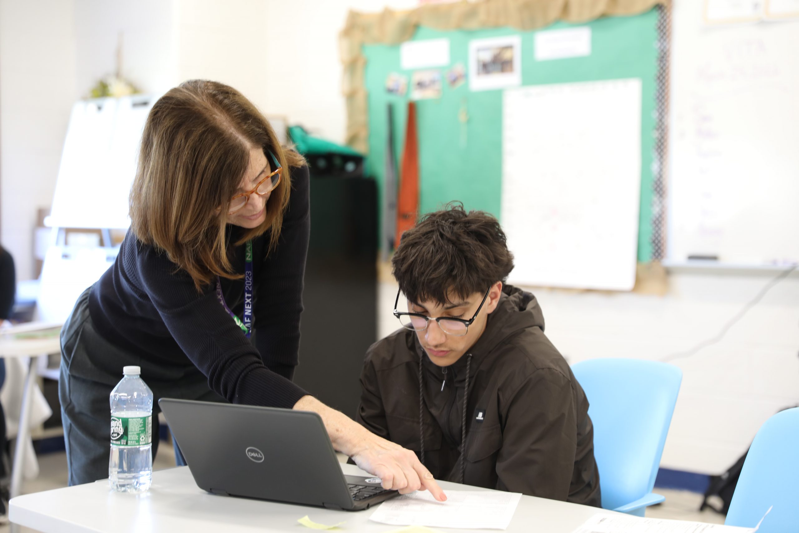 a teacher is leaning over a desk to assist a student