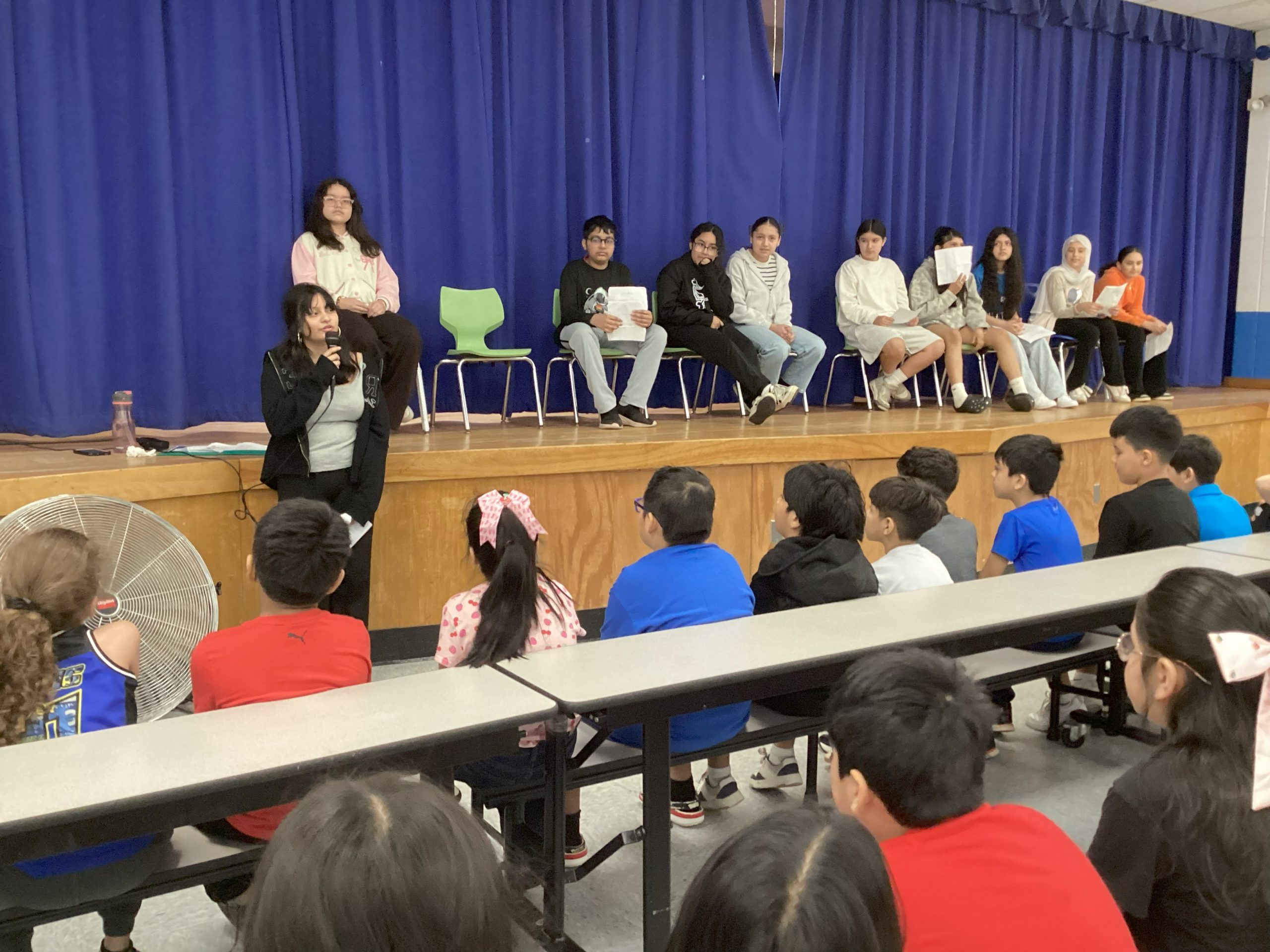 an older student speaks to a group of younger students in the cafeteria