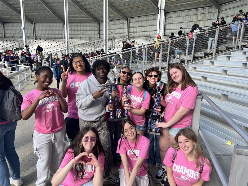 a group of students wearing pink shirts pose holding the trophy they earned at Music in the Parks