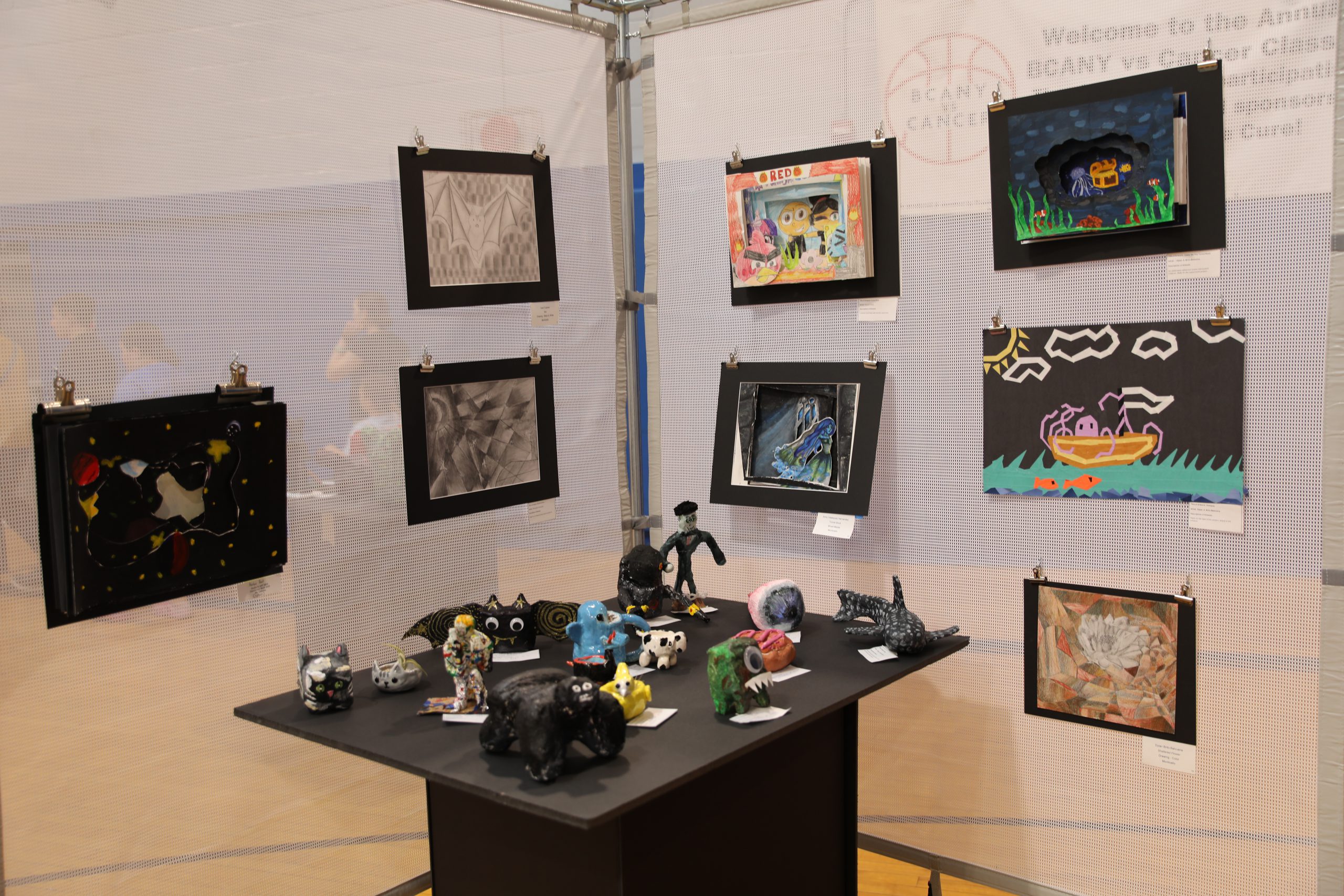 a photo of one of the exihibits at the gallery. There are chalk drawings hanging on the temporary walls, and there is a table with student sculptures