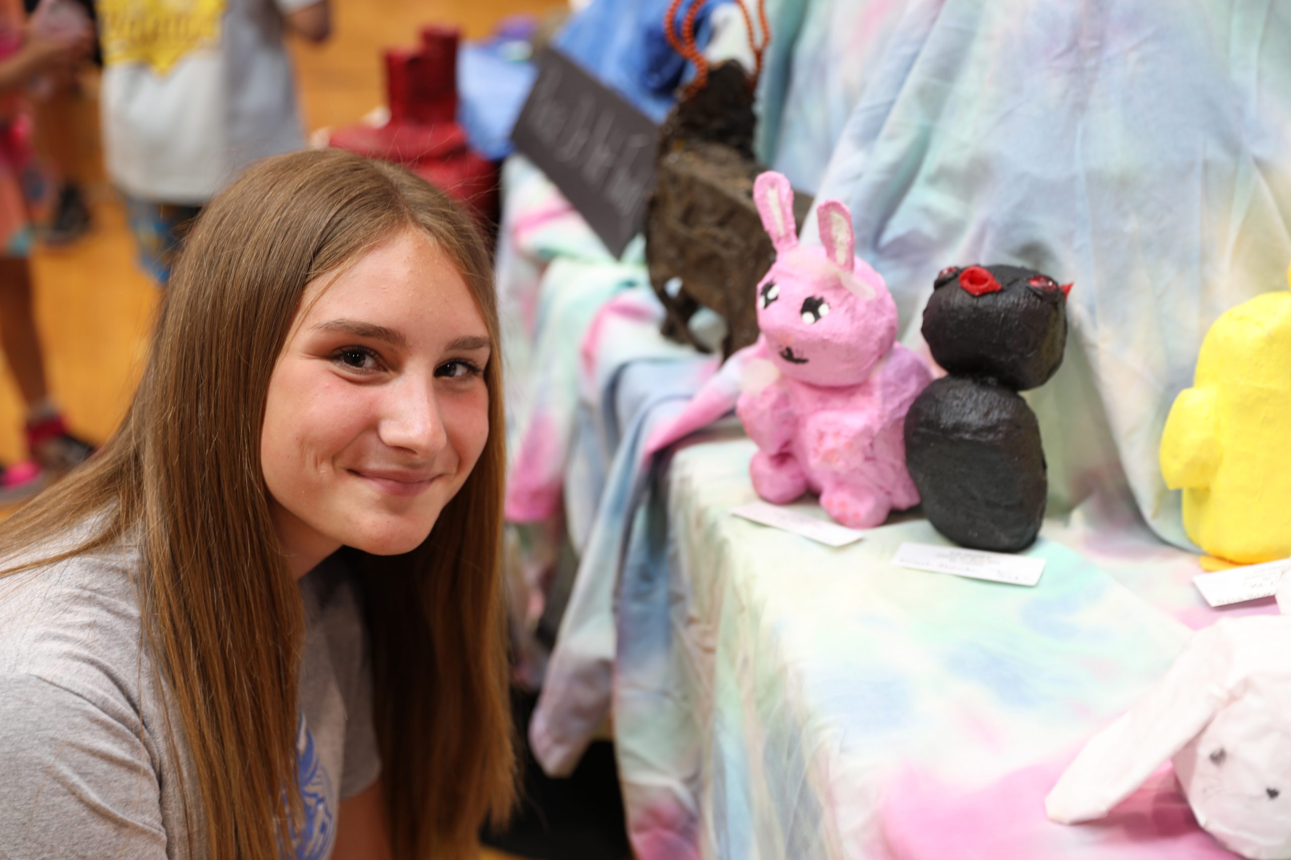 a teenage students poses next to a sculpture of a pink bunny she created