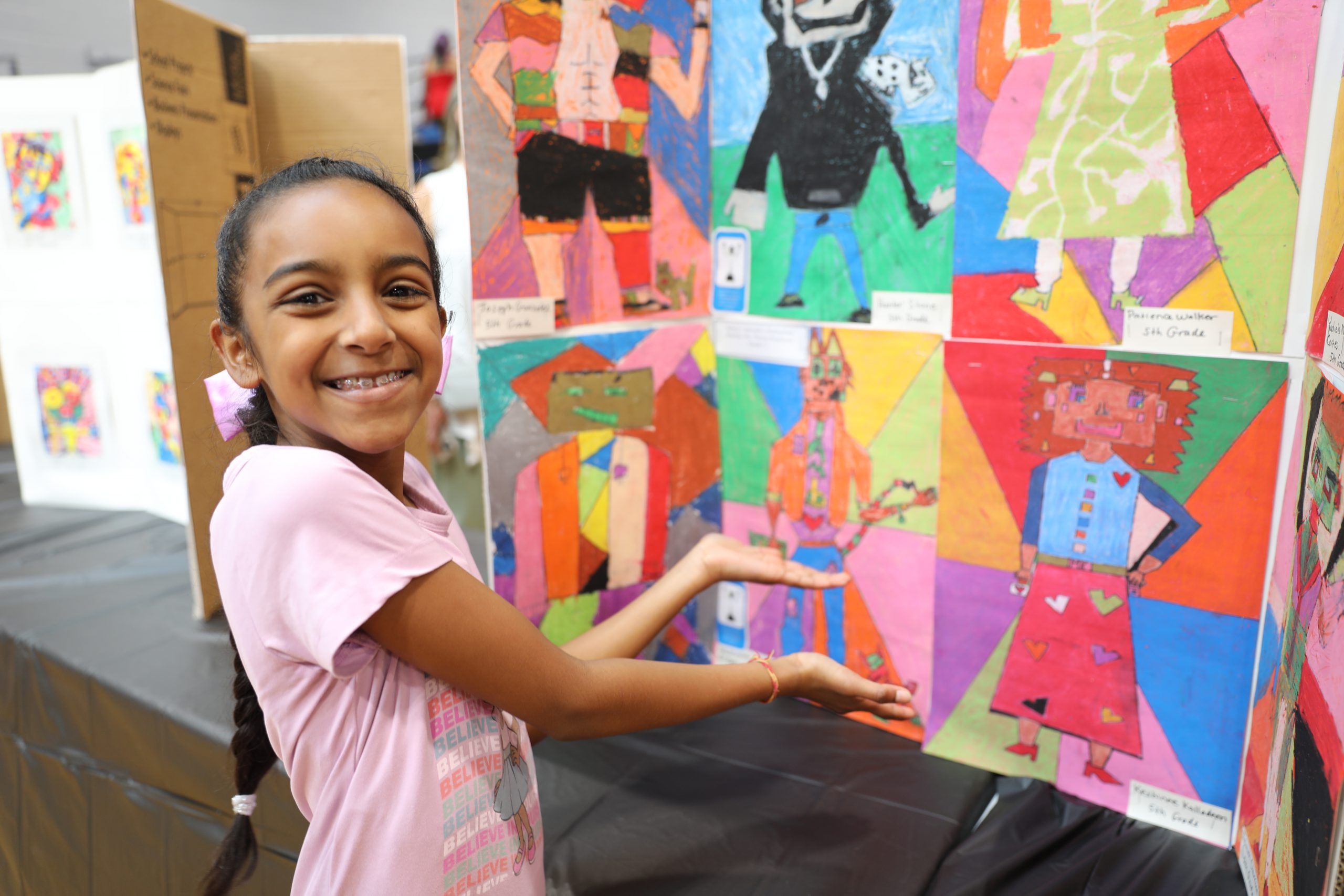 a student stands next to her artwork, which is a bright and colorful mixed media piece