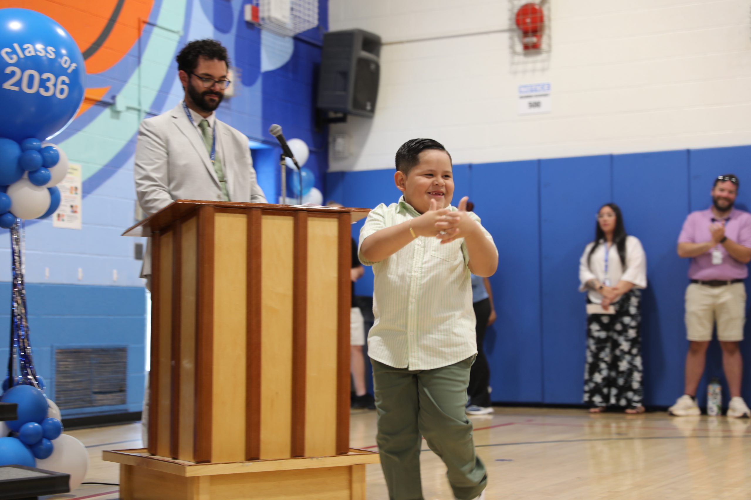 a young boy gives a thumbs up to the audience as he walks to receive his certificate 