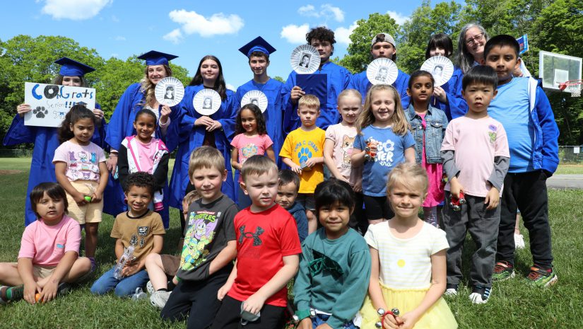 a group of kindergarten and senior students are gathered together and posing for a photo
