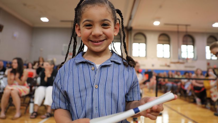a preschooler smiles for the camera while holding his diploma