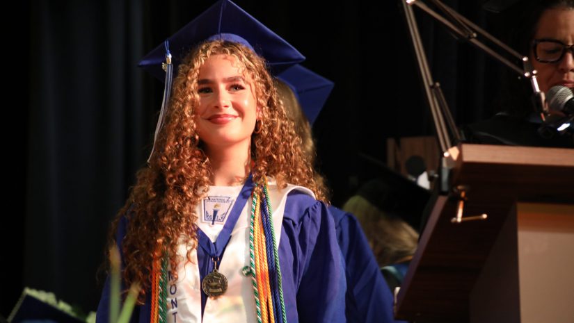 a graduate smiles at the audience while waiting to receive her diploma